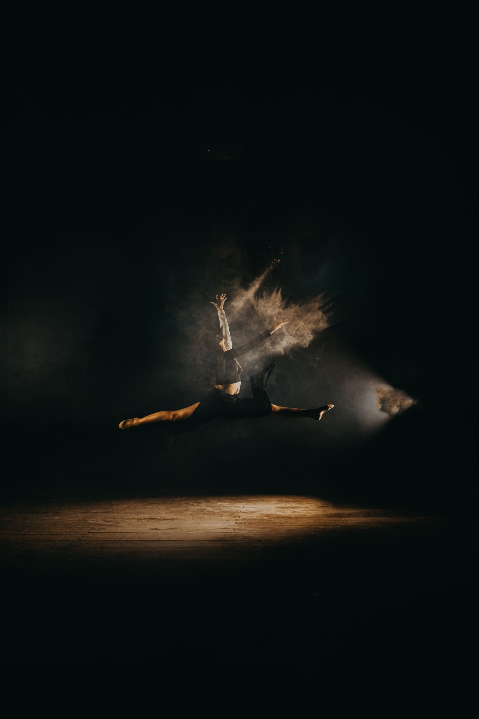 Dancer in a spotlit split leap surrounded by golden dust