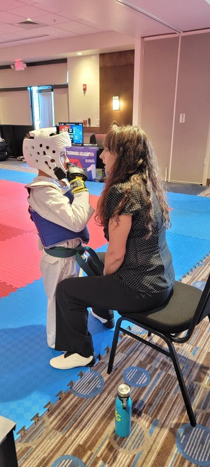 Master Sara Whatley coaching a young student ringside at a taekwondo tournament