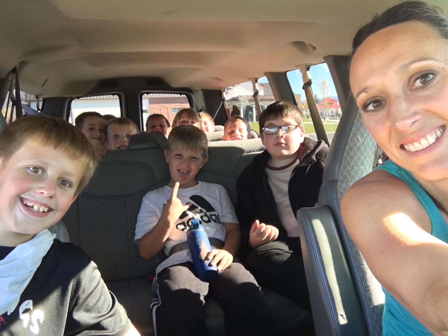 A smiling instructor takes a selfie with a van full of grinning kids on the after school pickup run